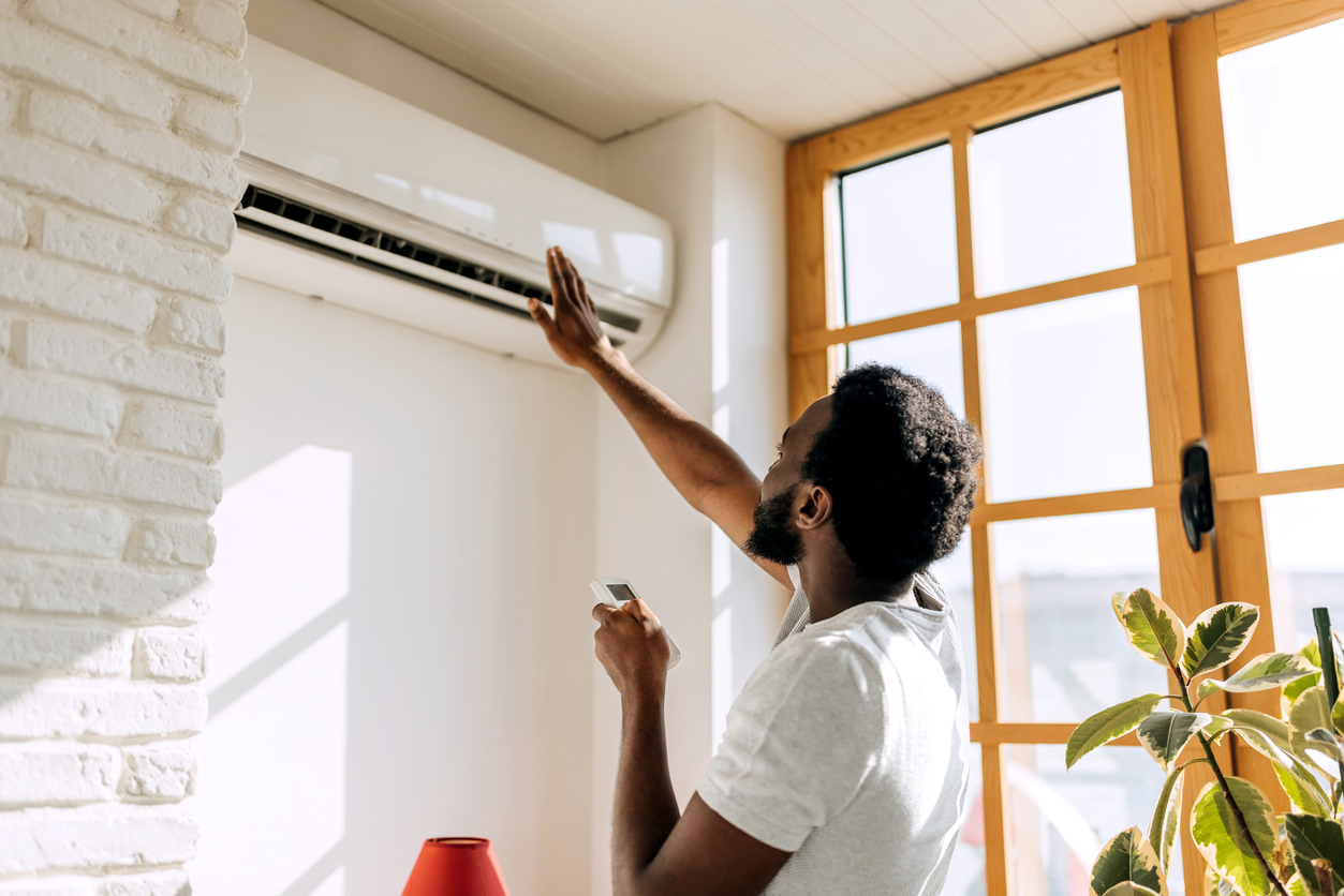 Man holding remote, holding his hand up to check the airflow of his ductless air conditioner in his home in San Jose, CA.